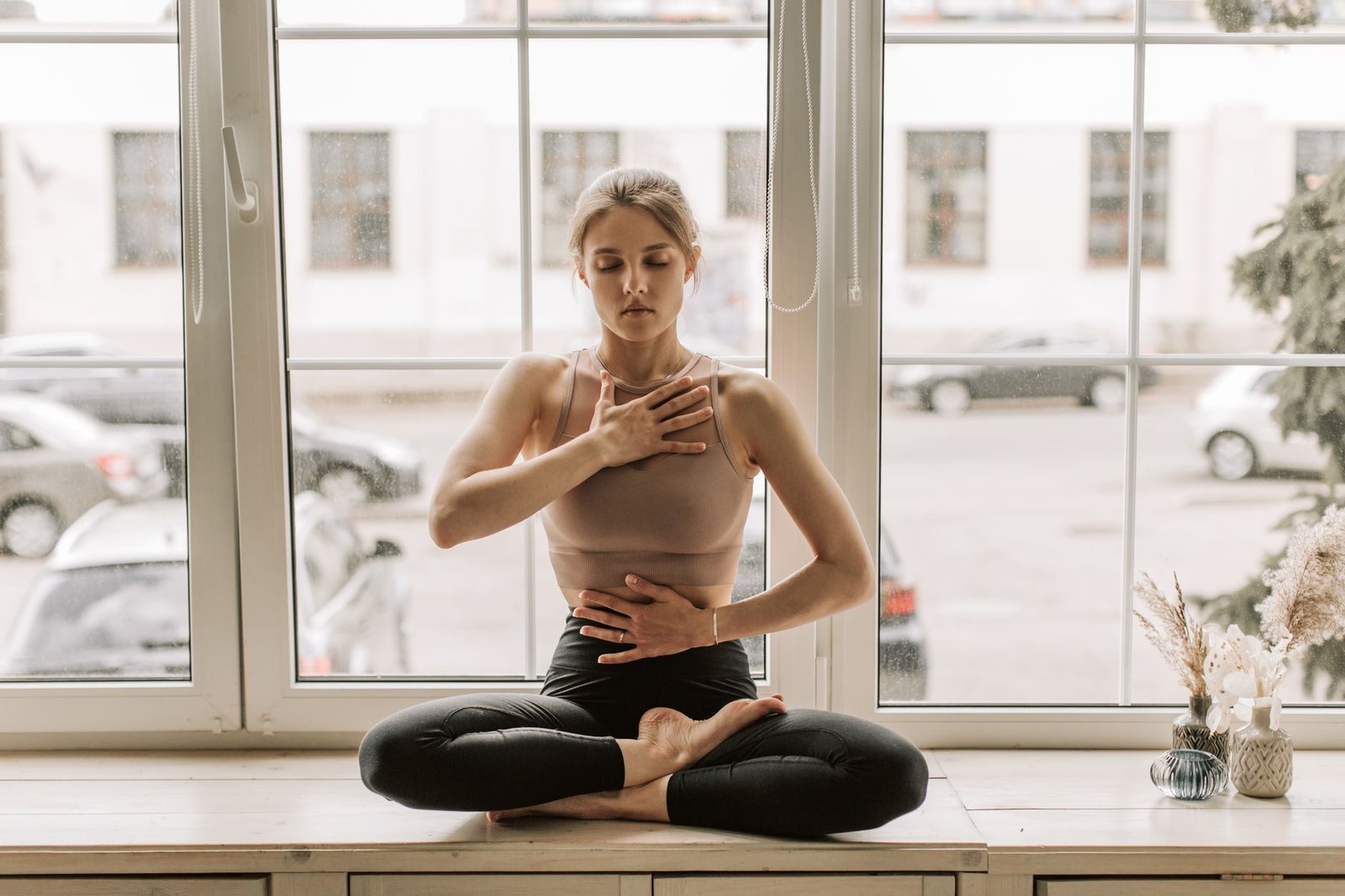 Woman sitting by a window with hand on her chest, doing somatic breathwork for grief and loss