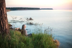 Woman sitting quietly by the water practicing present-moment mindfulness meditation