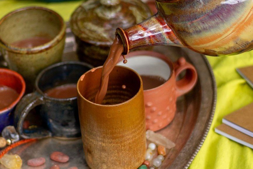 Ceremonial cacao being poured into handmade clay cups as part of a ritual preparation